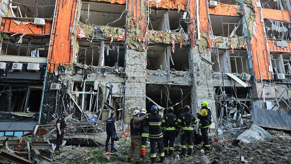 Rettungskräfte stehen in Charkiw in der Ukraine vor einem Bürogebäude, das durch einen russischen Raketenangriff zerstört wurde. © dpa-Bildfunk/Ukrinform 