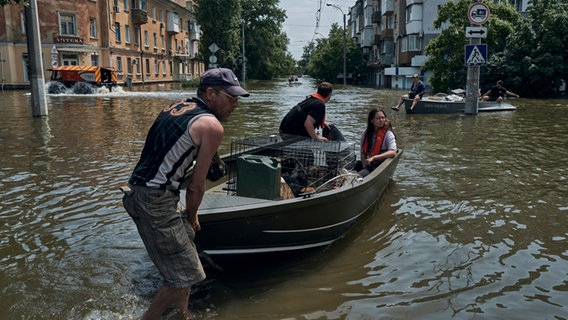 Menschen mit Haustieren werden mit einem Boot aus einem überfluteten Stadtteil der ukrainischen Stadt Cherson evakuiert. © LIBKOS/AP/dpa 