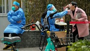 Eine Frau hebt ihre Maske, um einen Abstrich für einen Covid-Test in Peking zu machen. © dpa bildfunk/AP Foto: Ng Han Guan