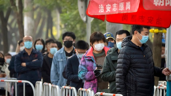 Menschen mit Mund-Nasen-Schutz stehen in Peking Schlange vor einem Corona-Testzentrum. © picture alliance/dpa/AP Foto: Mark Schiefelbein