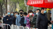Menschen mit Mund-Nasen-Schutz stehen in Peking Schlange vor einem Corona-Testzentrum. © picture alliance/dpa/AP Foto: Mark Schiefelbein