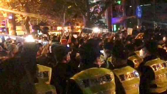 In diesem Bild aus einem Video, das The Associated Press erhalten hat, beobachtet die Polizei die Demonstranten in Shanghai. © Uncredited/AP/dpa 