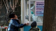 Ein Arbeiter in Schutzkleidung nimmt in Peking eine Corona-Probe von einem Bewohner ab © Andy Wong/AP/dpa 