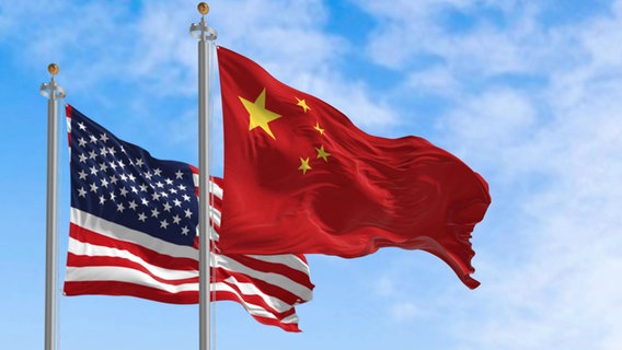Die Nationalflaggen von China und von den USA wehen im Wind. © IMAGO / Zoonar 
