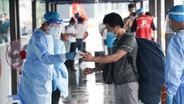Mitarbeiter überprüfen im Bahnhof Nanjing in der ostchinesischen Provinz Jiangsu die Personalien und den Gesundheitscode eines Fahrgastes. © dpa-Bildfunk 