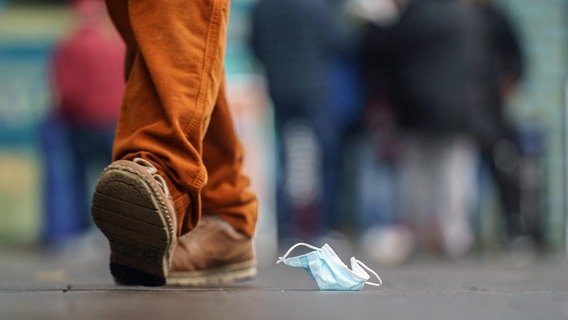 Ein Mann geht an einer auf dem Boden liegenden OP-Maske vorbei. © dpa-Bildfunk Foto: Frank Rumpenhorst