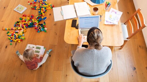 Ein zweijähriges Kind spielt im Wohnzimmer, während seine Mutter Zuhause im Homeoffice an einem Laptop arbeitet. © picture alliance/dpa | Julian Stratenschulte Foto: Julian Stratenschulte