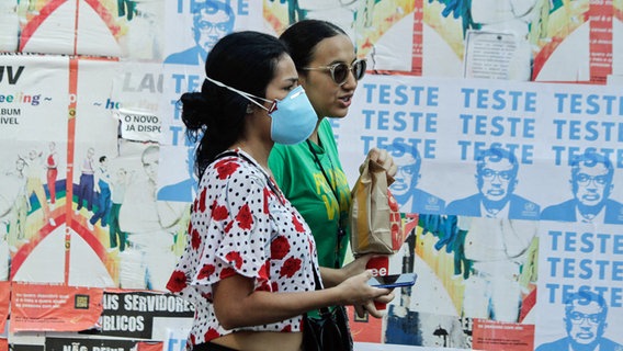 Zwei Frauen laufen in der brasilianischen Metropole Sao Paulo an Plakaten mit dem Konterfei des WHO-Generaldirektors Tedros Adhanom Ghebreyesus vorüber. Auf den Plakaten wird zum Testen auf das Coronavirus aufgerufen. (Foto vom 4. April 2020) © picture alliance / ZUMAPRESS.com | FÃÂ¡Bio Vieira/Fotorua 