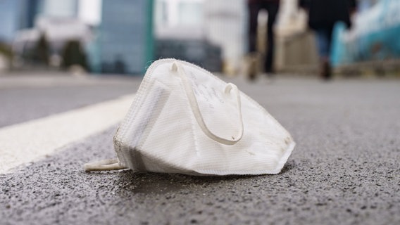 Eine Corona-Maske liegt auf einem nassen Gehweg. © dpa Foto: Frank Rumpenhorst
