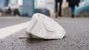 Eine Corona-Maske liegt auf einem nassen Gehweg. © dpa Foto: Frank Rumpenhorst