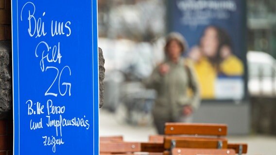 Ein Schild mit der Aufschrift "Bei uns gilt 2G - Bitte Perso und Impfausweis zeigen" hängt an einer Gaststätte in Hannover. © dpa-Bildfunk 