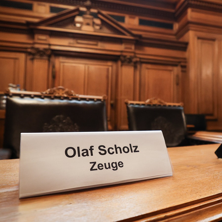 Ein Schild mit dem Text "Olaf Scholz Zeuge" steht auf einem Platz auf der Senatsbank vor Beginn einer Sitzung des Parlamentarischen Untersuchungsausschusses "Cum-Ex" im Plenarsaal der Hamburgischen Bürgerschaft im Rathaus. © picture alliance/dpa Foto: Christian Charisius