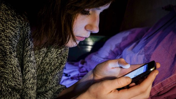 Ein Mädchen liegt auf einem Bett und schaut auf ihr Handy. © imago/Reporters Foto: imago stock&people