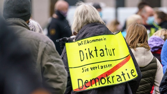 Eine Demonstrantin steht bei einer Kundgebung der "Querdenken"-Bewegung mit einem Plakat mit der Aufschrift "Willkommen in Diktatur - Sie verlassen Demokratie", das einem Ortsschild nachempfunden ist. © dpa bildfunk Foto: Frank Rumpenhorst