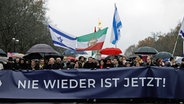 Teilnehmer einer Demonstration protestieren unter dem Motto "Deutschland steht auf - Nie wieder ist jetzt!" gegen Antisemitismus. In der ersten Reihe halten unter anderem Rabbi Jehuda Teichtal, Bundestagspräsidentin Bärbel Bas (SPD), Musiker Roland Kaiser, Publizist Michel Friedman, Berlins Oberbürgermeister Kai Wegner (CDU), Grünen-Vorsitzende Ricarda Lang und Bundesarbeitsminister Hubertus Heil (SPD) ein Plakat mit der Aufschrift "Nie wieder ist jetzt". © Carsten Koall/dpa 