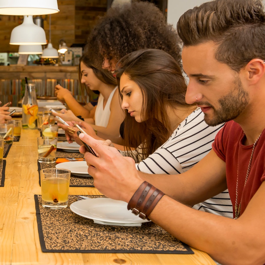 Eine Gruppe junger Leute sitzt an einem langen Tisch und jeder schaut auf sein Smartphone. © Colourbox Foto: Ikostudio