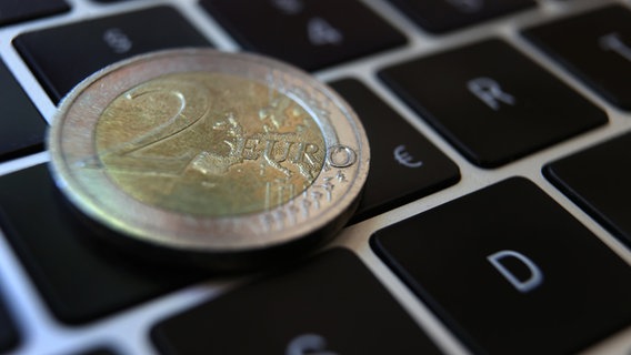 Eine Zwei-Euro-Münze liegt auf der Tastatur eines Laptops. © Karl-Josef Hildenbrand/dpa 