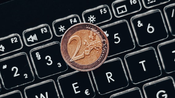 Ein Zwei-Euro-Stück liegt auf der Tastatur eines Laptops. © IMAGO / aal.photo 