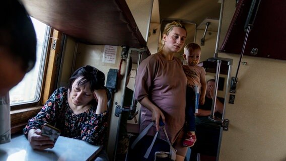 Eine Frau mit einem kleinen Kind auf dem Arm sucht einen Sitzplatz im Zug, der sie von Pokrowsk in der Region Donezk in der Ostukraine in einen sichereren Teil des Landes im Westen bringen soll. © David Goldman/AP/dpa 