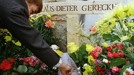Ein Mann legt am 29.06.2000 in Greifswald an das Kreuz für den umgebrachten Obdachlosen Klaus-Dieter Gerecke neben Kerzen und Blumen ein Foto nieder. © picture-alliance / ZB Foto: Stefan Sauer