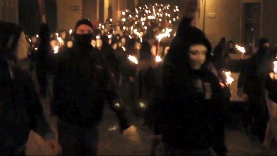 Maskierte Menschen marschieren mit Fackeln.  
