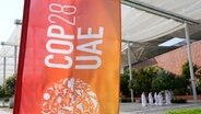 Eine Fahne mit dem Logo der Weltklimakonferenz (COP28) weht vor dem Veranstaltungsort in Dubai. © Rafiq Maqbool/AP/dpa 