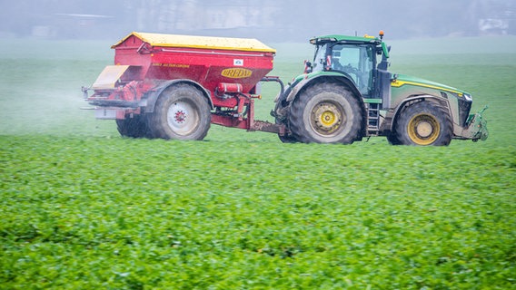 Ein Traktor fährt mit einem Streuwagen über ein Feld und bringt Dünger aus. © picture alliance/dpa | Foto: Jens Büttner