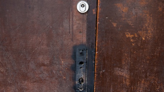 Eine braune Tür mit einem kaputten schwarzen Schloss und einem darüber installierten neuen Schloss © Picture Alliance/dpa Foto: Daniel Bockwoldt