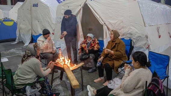 Überlebende des Erdbebens in der türkischen Stadt Adana wärmen sich an einem Feuer. © picture alliance / ZUMAPRESS.com Foto: Tolga Ildun