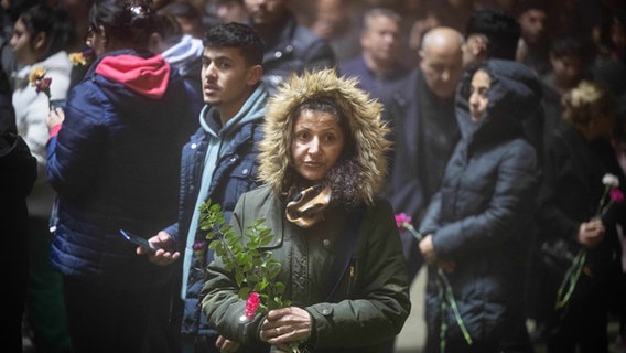 Eine Frau steht im Vordergrund mit einer Blume in der Hand, hinter ihr stehen weitere Menschen. © Boris Roessler/dpa Foto: Boris Roessler
