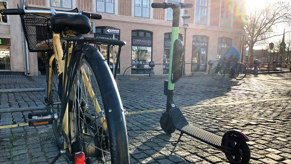 Ein Fahrrad steht auf einem gepflasterten Platz neben einem Elektro-Roller. © dpa picture alliance Foto: Steffen Trumpf