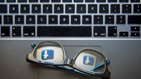 In einer Brille die auf einem Laptop liegt spiegelt sich das Logo von Facebook. © dpa bildfunk Foto: Dominic Lipinski