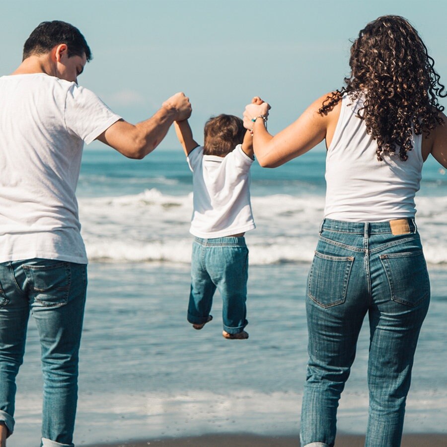 Ein Elternpaar hält sein kleines Kind am Strand an den Händen und lässt es fliegen © Colorbox Foto: Oleksandr Latkun