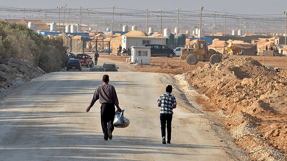 Syrische Flüchtlinge gehen auf einer Straße. Im Hintergrund ein Auffanglager in Jordanien. © dpa picture alliance Foto: Yann Foreix