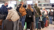 Reisende stehen auf dem Flughafen Hamburg an einem Check-In-Schalter an. © picture alliance/dpa Foto: Bodo Marks