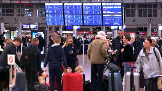Flugreisende stehen vor den Anzeigetafeln im Terminal 1 am Airport Hamburg. © Christian Charisius, dpa 