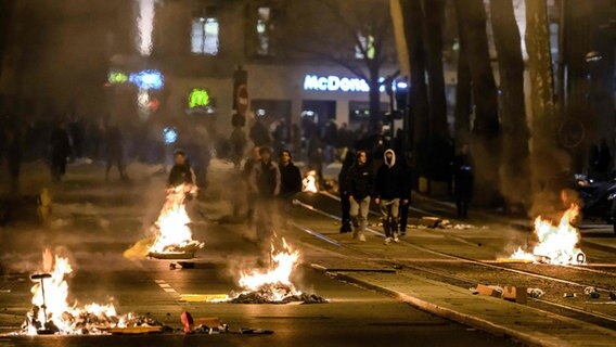 Lyon: Menschen gehen während einer Demonstration an brennenden Abfällen auf einer Straße vorbei. © Jeff Pachoud/AFP/dpa 