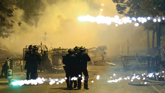 Beamte der Bereitschaftspolizei patrouillieren bei Unruhen auf einer Straße, während Feuerwerkskörper explodieren. © dpa Bildfunk Foto: Aurelien Morissard
