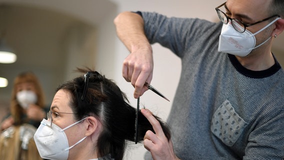 Ein Friseur schneidet einer Kundin die Haare, beide tragen FFP2-Masken. © dpa/APA Foto: Roland Schlager