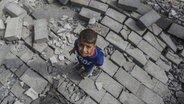 Palästinensische Gebiete, Flüchtlingslager Bureij: Ein palästinensisches Kind steht nach den israelischen Luftangriffen auf Überresten zerstörter Gebäude. © dpa Foto: Mohammed Talatene
