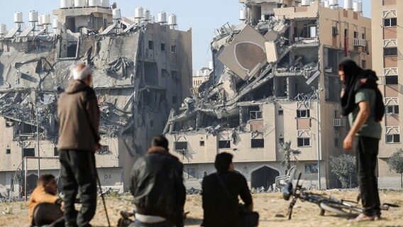 Bewohner eines Wohnkomplexes in Chan Junis im südlichen Gazastreifen sitzen nach einem israelischen Angriff vor den zerstörten Häusern. © dpa-Bildfunk/SOPA Images via ZUMA Press Wire Foto: Ahmed Zakot