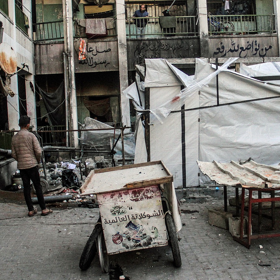 Mehrere Menschen begutachten die Schäden in einem ehemaligen Schulgebäude im Gazastreifen, in dem Flüchtlinge untergebracht waren. © dpa picture alliance/ZUMAPRESS Foto: Mahmoud Issa