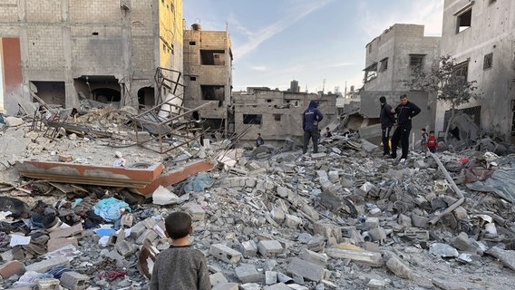 Mehrere Personen inspizieren zerstörte Gebäude im Gazastreifen. © picture alliance / Anadolu | Hasan N. H. Alzaanin Foto: Hasan N. H. Alzaanin