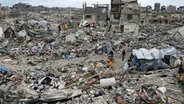 Menschen gehen im Gazastreifen durch Trümmer von Häusern, die durch Angriffe der israelischen Armee zerstört wurden. © dpa bildfunk/AP Foto: Abdel Kareem Hana