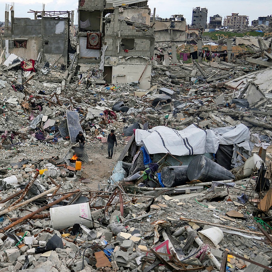 Menschen gehen im Gazastreifen durch Trümmer von Häusern, die durch Angriffe der israelischen Armee zerstört wurden. © dpa bildfunk/AP Foto: Abdel Kareem Hana