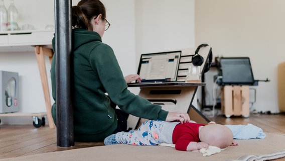 Eine Frau arbeitet am Rechner und streichelt dabei ihr Baby. © standsome worklifestyle via unsplash 