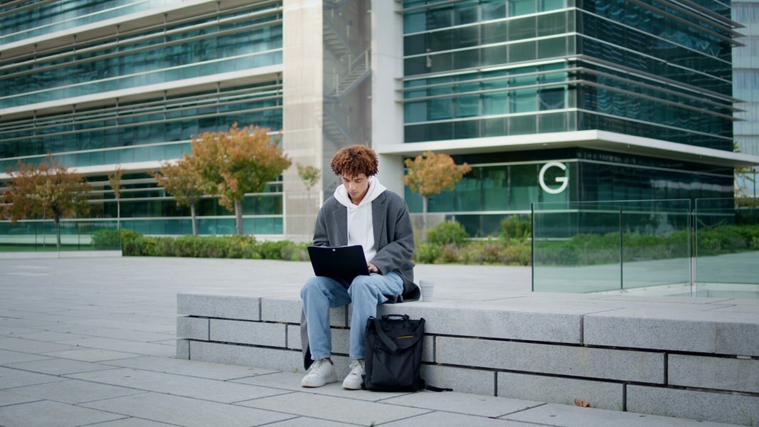 Ein junger Mann arbeitet auf einer Mauer an einem Laptop