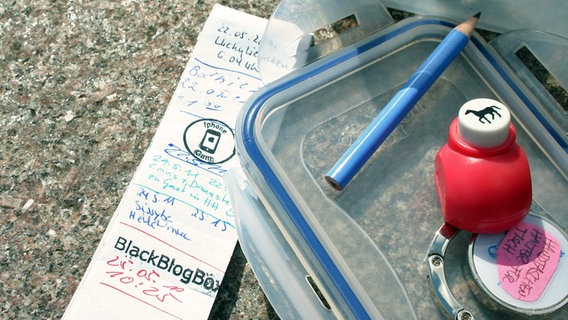 Tupperdeckel mit Stempel, Bleistift, Log-Buch fürs Geocaching © NDR Foto: Catherine Grim