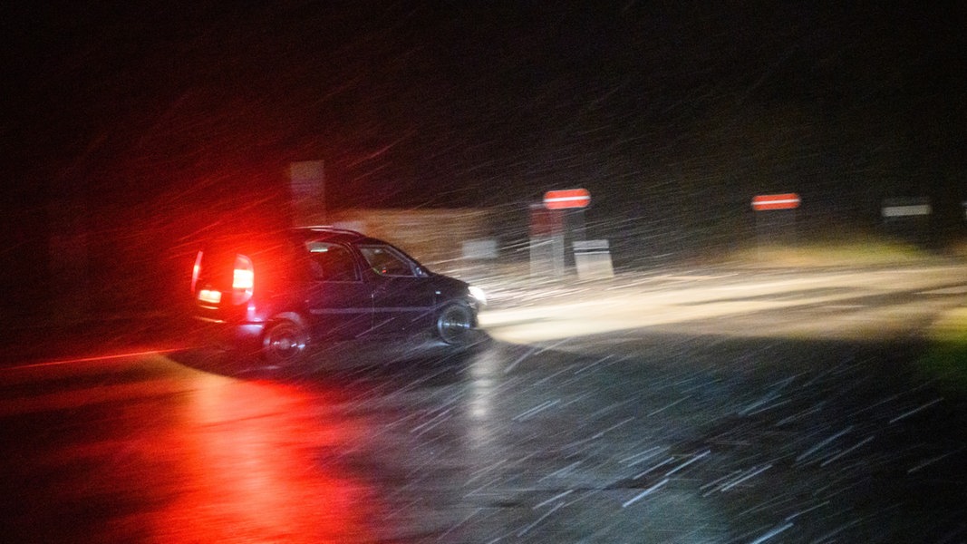 Ein Auto fährt in einem Schneeschauer über eine dunkle Straße.