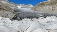 Helle Textilplanen decken Teile des Gletschers ab, um das Schmelzen zu verlangsamen. © ARD Foto: Kathrin Hondl